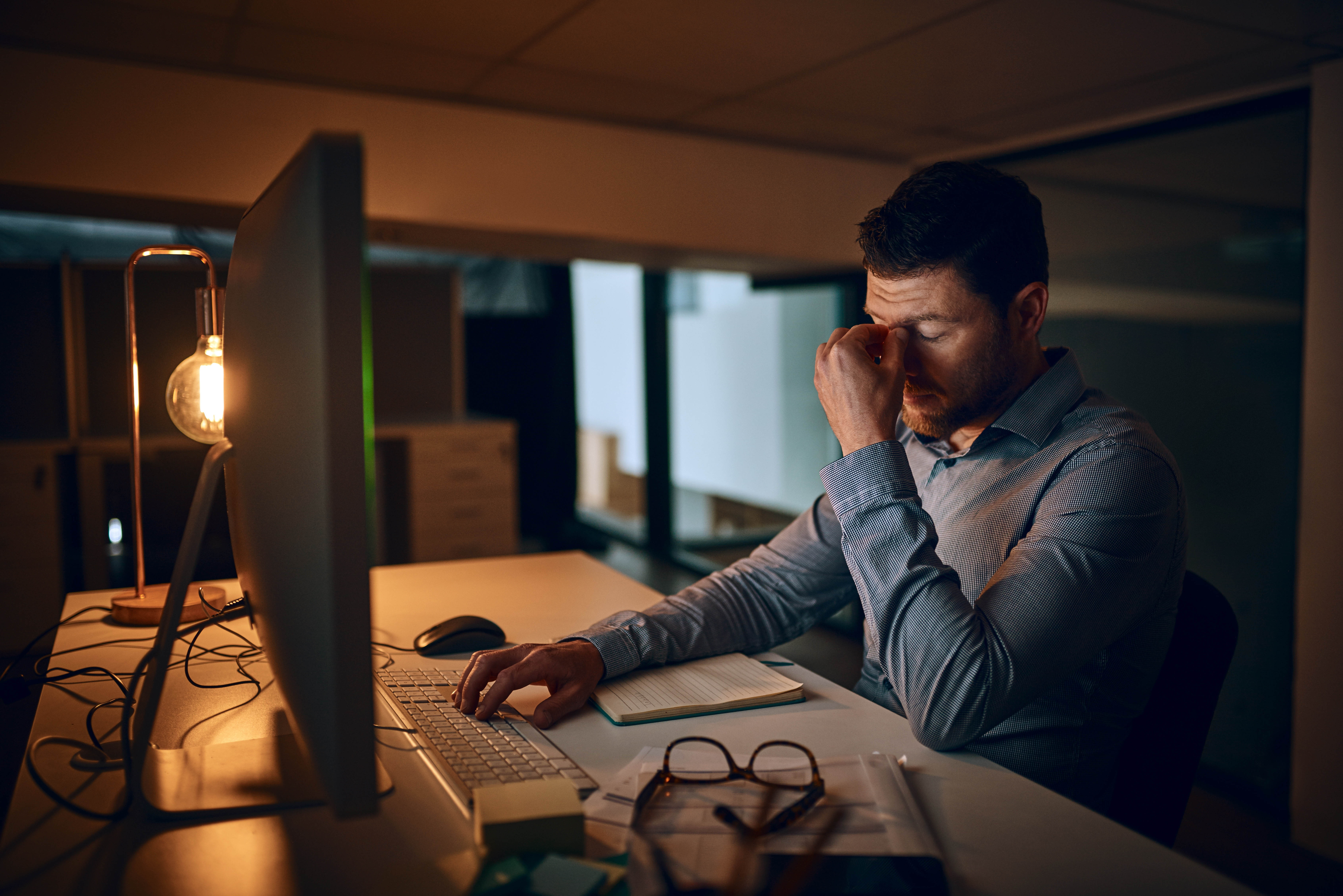 Man sitting in the dark in front of his computer, rubbing his eyes out of fatigue and tiredness Man sitting in the dark in front of his computer, rubbing his eyes out of fatigue and tiredness